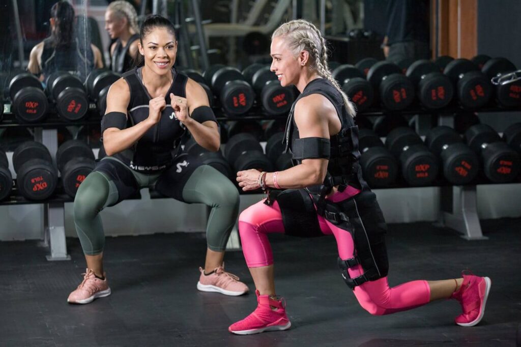 Two women performing strength and flexibility training next to dumbell weights