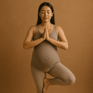 Pregnant woman in a comfortable skin-tight brown shaded outfit peacefully balancing on one leg with hands clasped together in prayer position | Pre & Postnatal Wellness